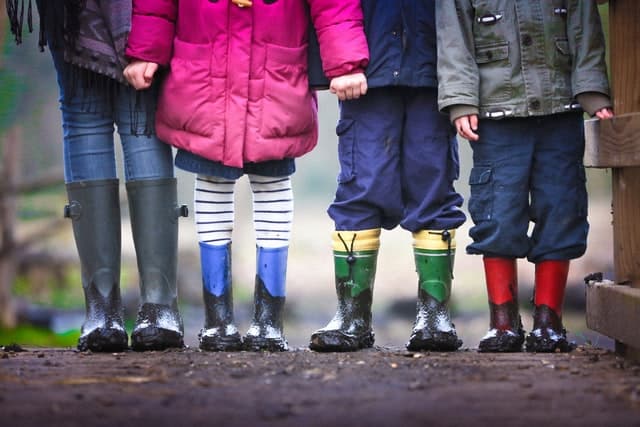 Four children depicted from their torsos down, wearing colorful coats and rain boots, ready for adventure in New Zealand.