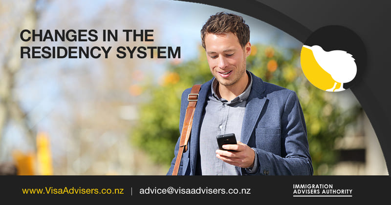 A man is standing with his phone in hand, engrossed in reading about the new changes in the residency system in New Zealand. His focused expression indicates his interest in understanding the updated policies and regulations.